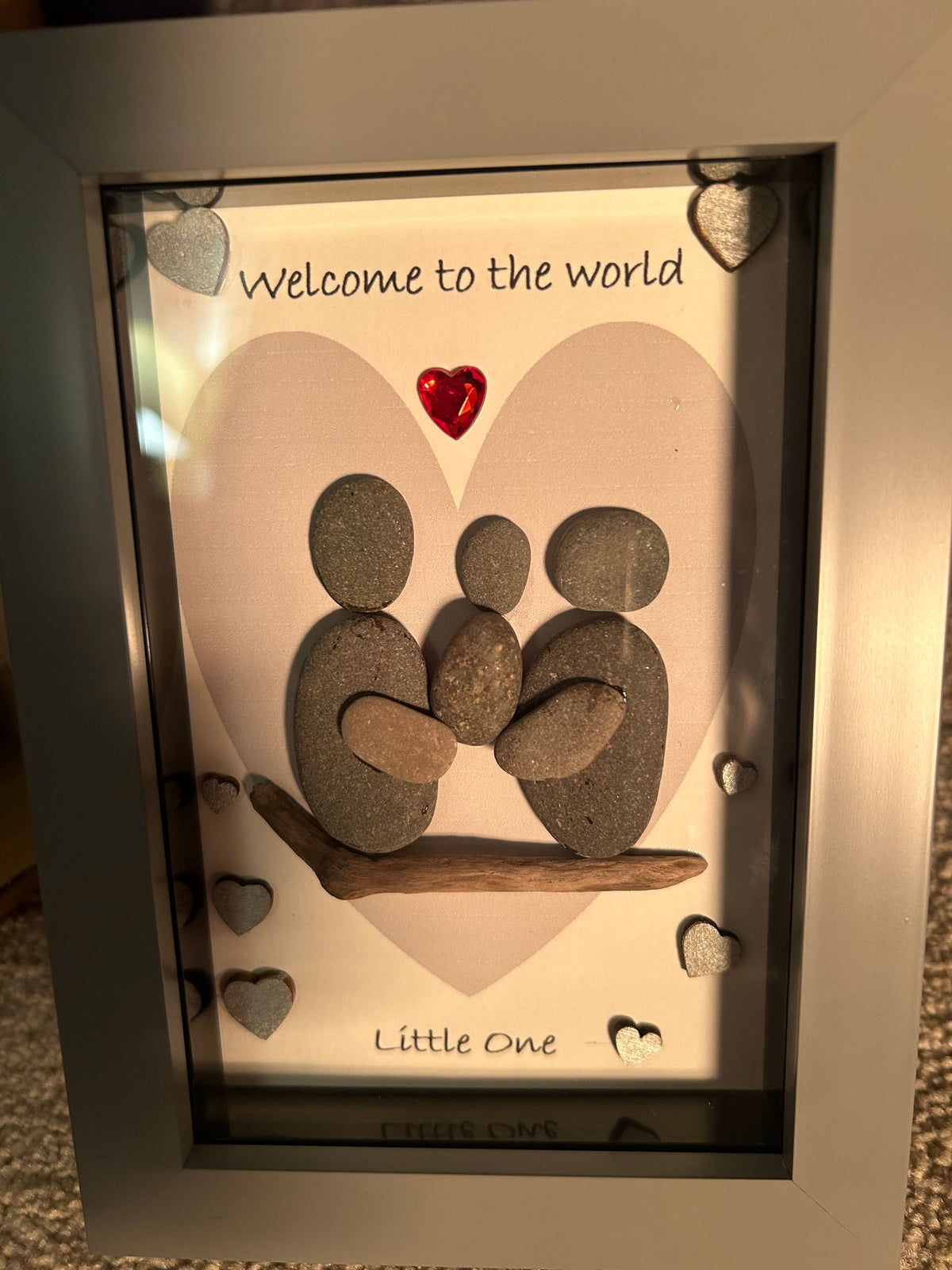 Two pebble parents cradling new baby on driftwood with welcome to the world little one quote shadow box frame