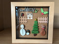 Festive Christmas pebble art scene with snowman, penguin, Christmas tree, gingerbread man and robin in a wooden frame