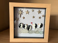 Penguin family pebble art with sea glass and golden stars in a wooden frame