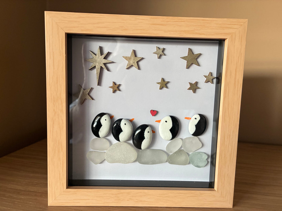 Penguin family pebble art with sea glass and golden stars in a wooden frame