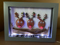 Three reindeer pebble art with sea glass baubles on antlers and LED fairy lights in a grey frame