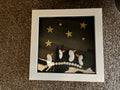 Handmade pebble art frame featuring three penguin figures under gold stars with Merry Christmas pebble lettering
