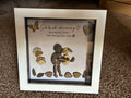 Side by side pebble art shadow box frame featuring a pebble person holding a pebble dog, with golden wooden paw prints, leaves, butterfly and heart embellishments, in a white frame