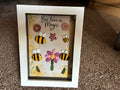 Bee-lieve in Magic pebble art shadow box frame with four hand-painted bee pebbles, a pink pebble daisy, and wooden flower embellishments on a watercolour botanical background, in a white frame